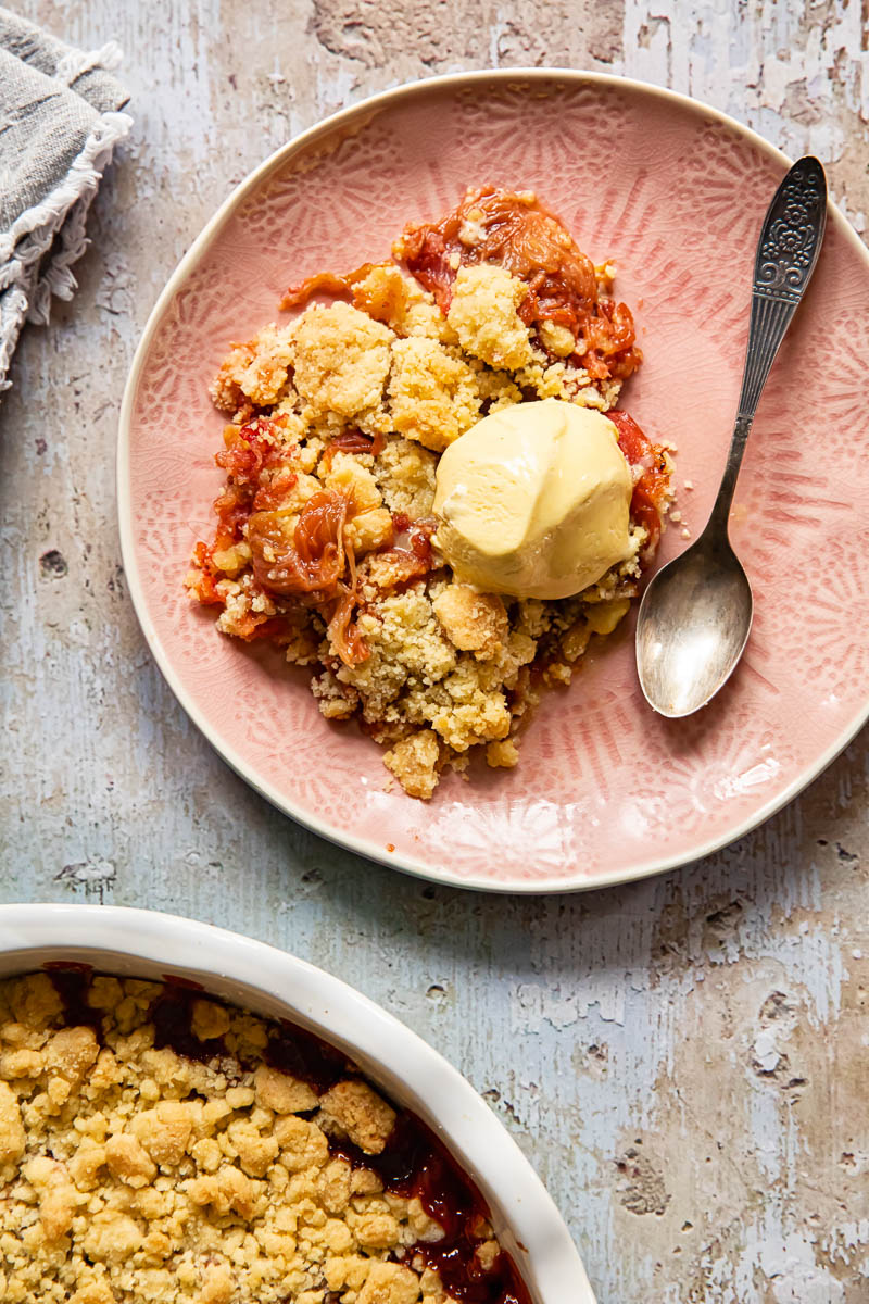 top down view of rhubarb crumble on a pink plate served with a scoop of vanilla ice cream