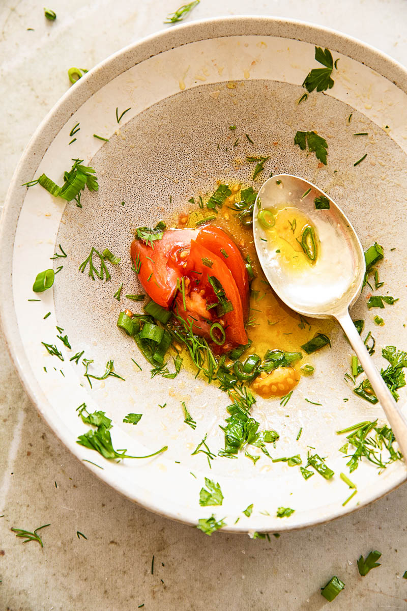 nearly empty salad bowl with salad dressing a tomato slice at the bottom, a spoon