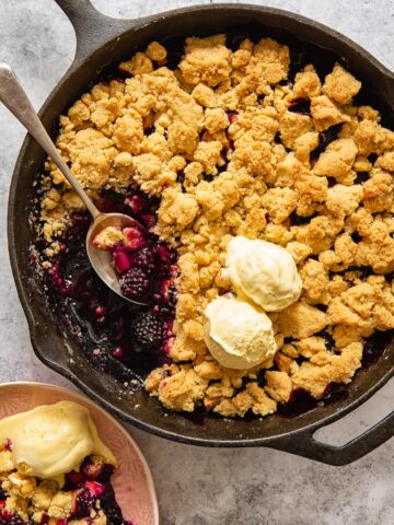 top down view of apple blackberry crumble in a pan topped with two scoops of vanilla ice cream
