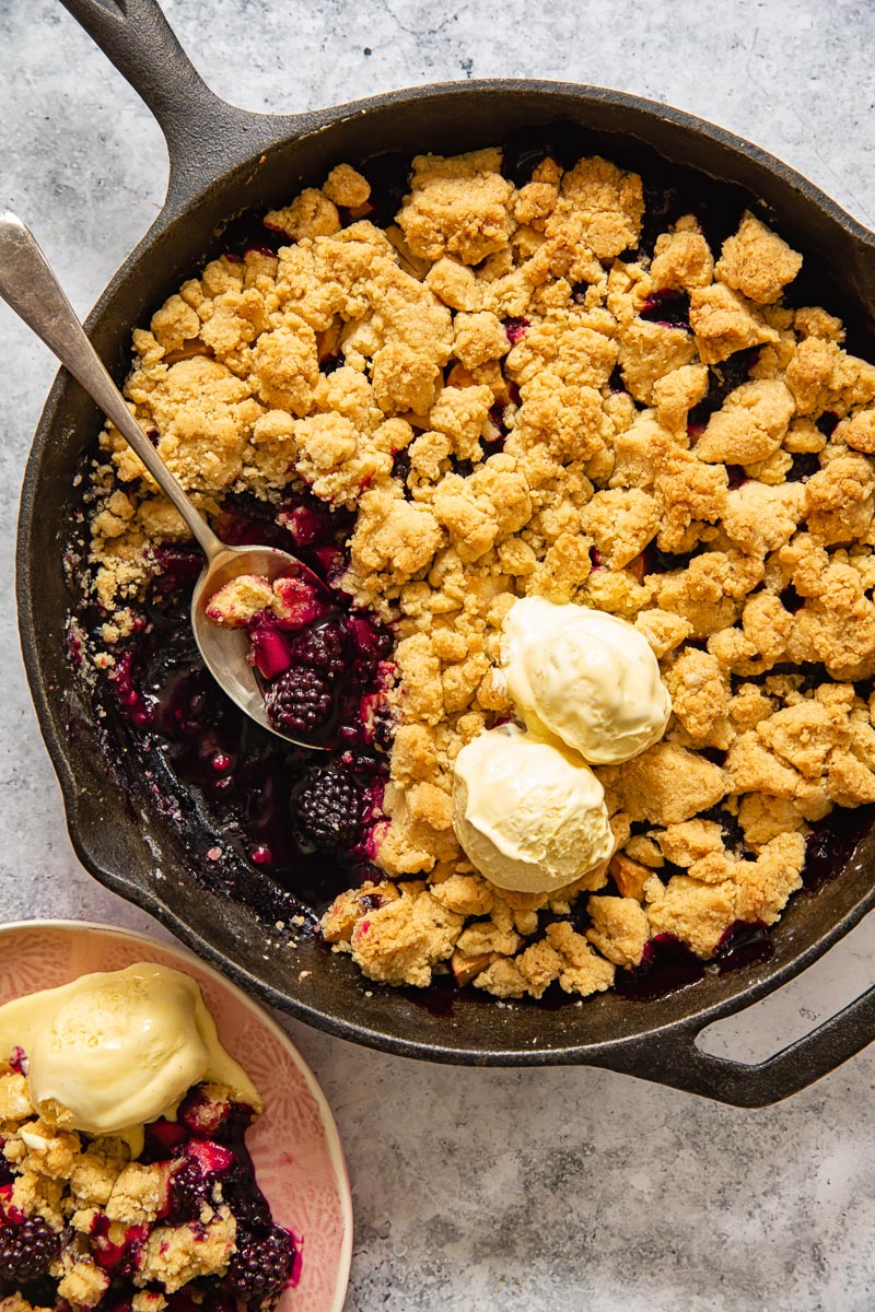 top down view of apple blackberry crumble in a pan topped with two scoops of vanilla ice cream