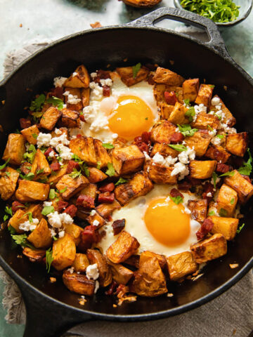 top down view of a skillet with diced potatoes, chorizo and egg with feta