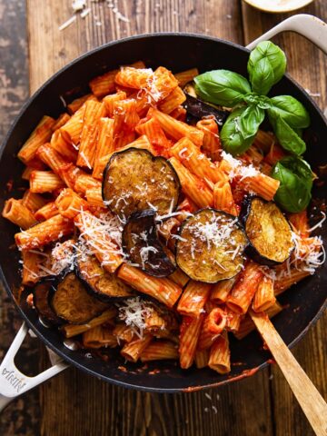 top down view of rigatoni with tomato sauce, topped with sliced of fried eggplant and grated Parmesan