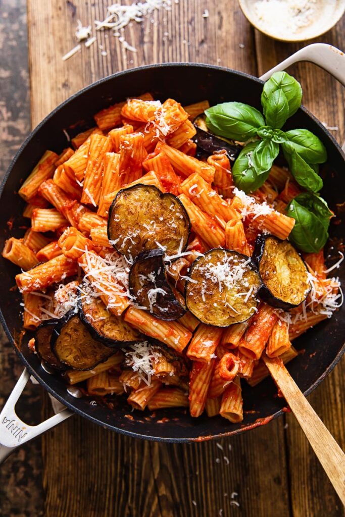 top down view of rigatoni with tomato sauce, topped with sliced of fried eggplant and grated Parmesan