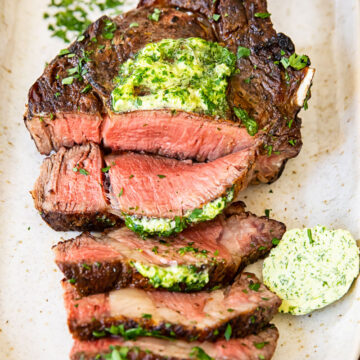 top down view of grilled and sliced steak on a platter, topped with herb butter