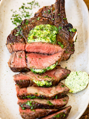 top down view of grilled and sliced steak on a platter, topped with herb butter