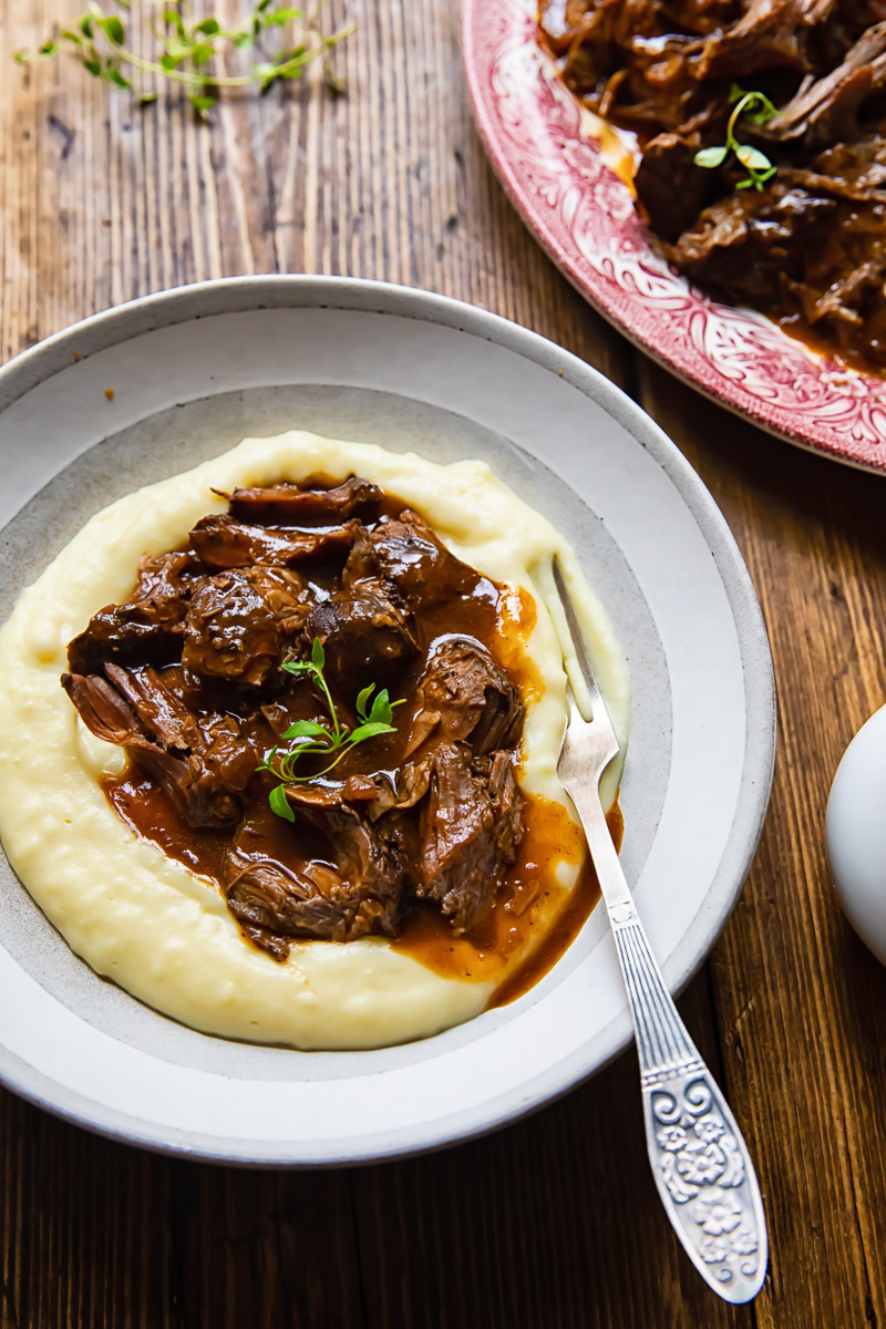 chunks of lamb with gravy on top of mashed potatoes in a bowl