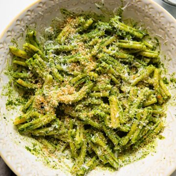 pesto pasta in a serving bowl with grated parmesan next to it