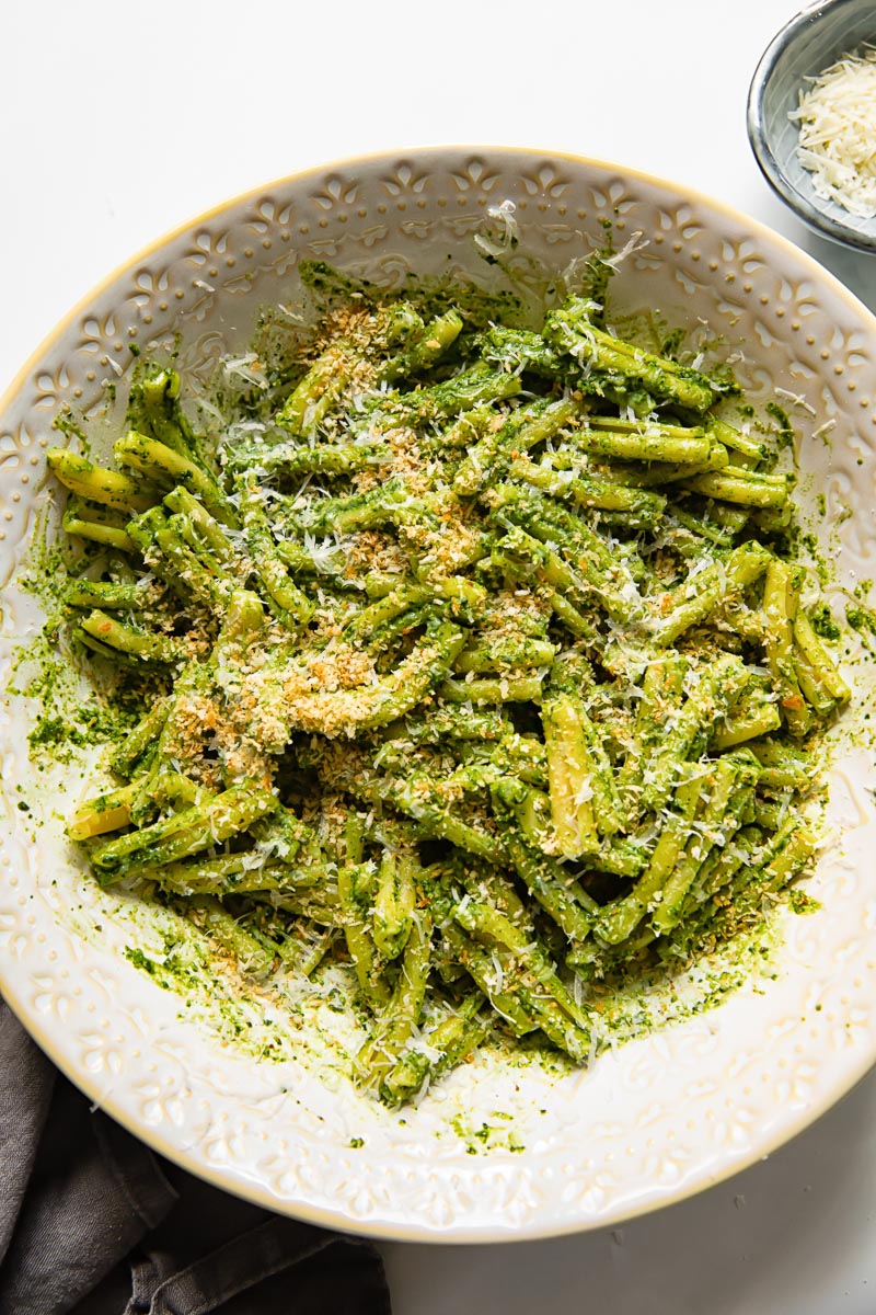 pesto pasta in a serving bowl with grated parmesan next to it