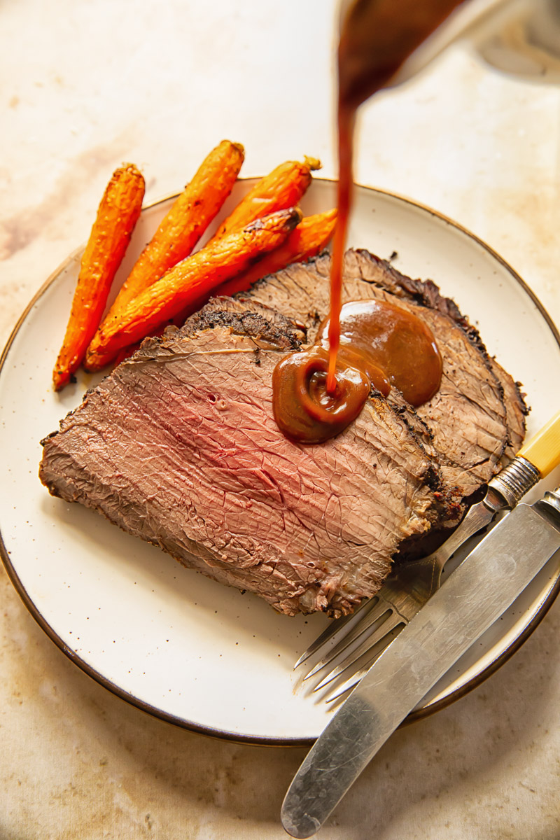 gravy is being poured on slices of roast beef on a plate