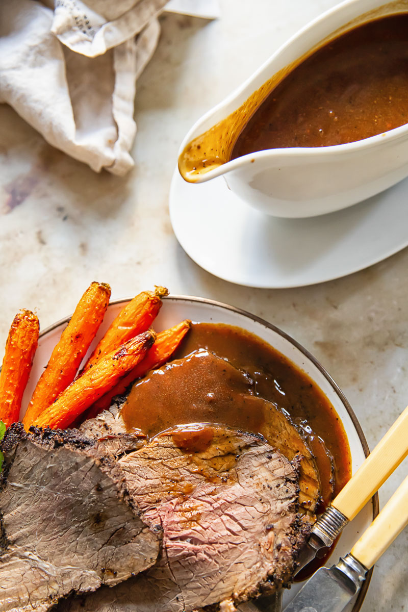 top down view of sliced roast beef with gravy and carrots on a plate, gravy boat with gravy in it