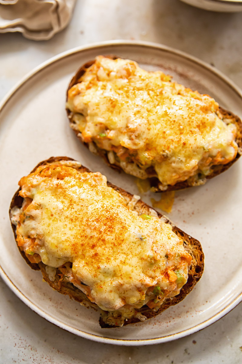 two pieces of bread on a plate with melted cheese and salmon