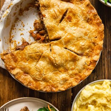 Pie with piece removed alongside salad and potatoes