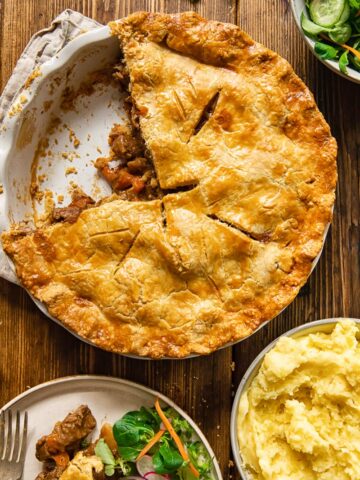 Pie with piece removed alongside salad and potatoes