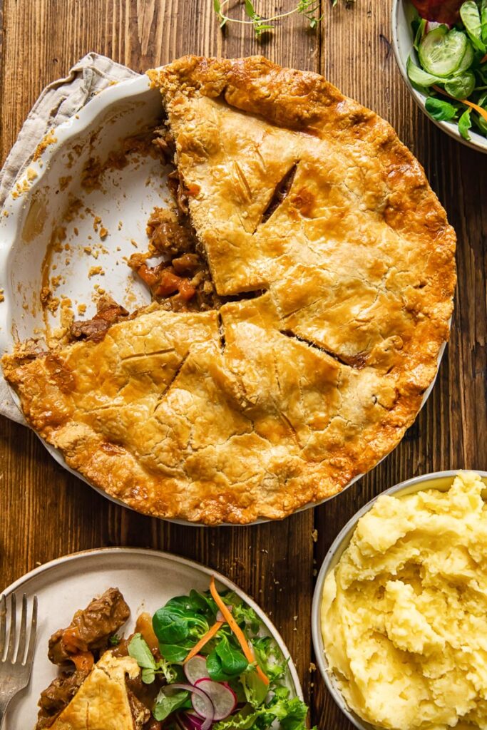 Pie with piece removed alongside salad and potatoes