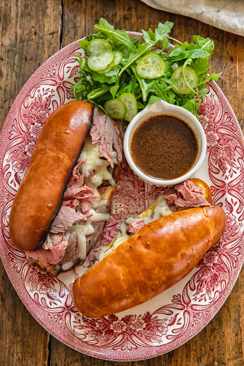 top down view of two French Dip Sandwiches on a platter with a little dish of jus and a green salad