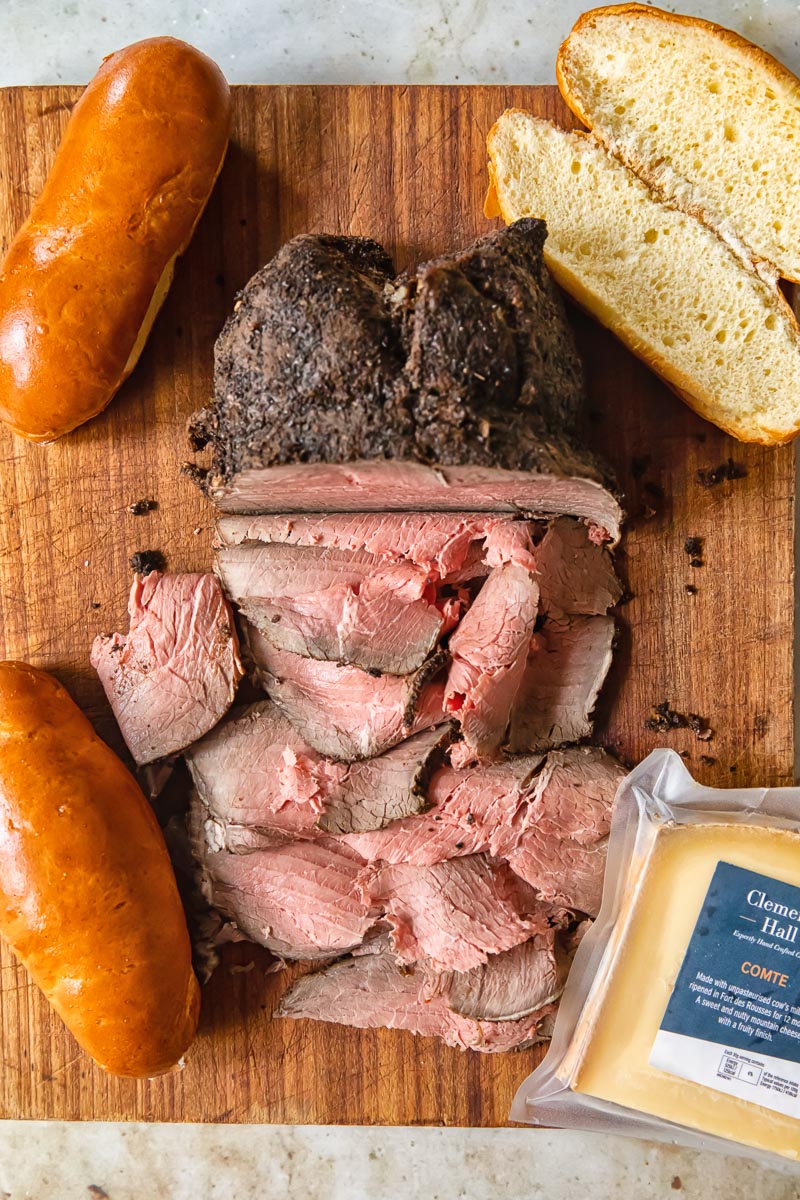 sliced roast beef, buns and a block of cheese on a cutting board