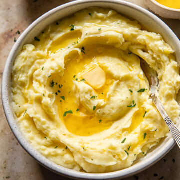 top down view of mashed potatoes drizzled with melted butter and chopped parsley in a bowl