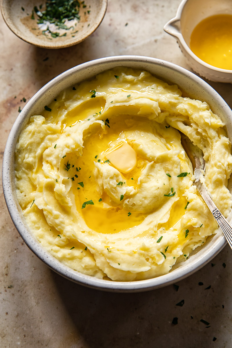 top down view of mashed potatoes drizzled with melted butter and chopped parsley in a bowl