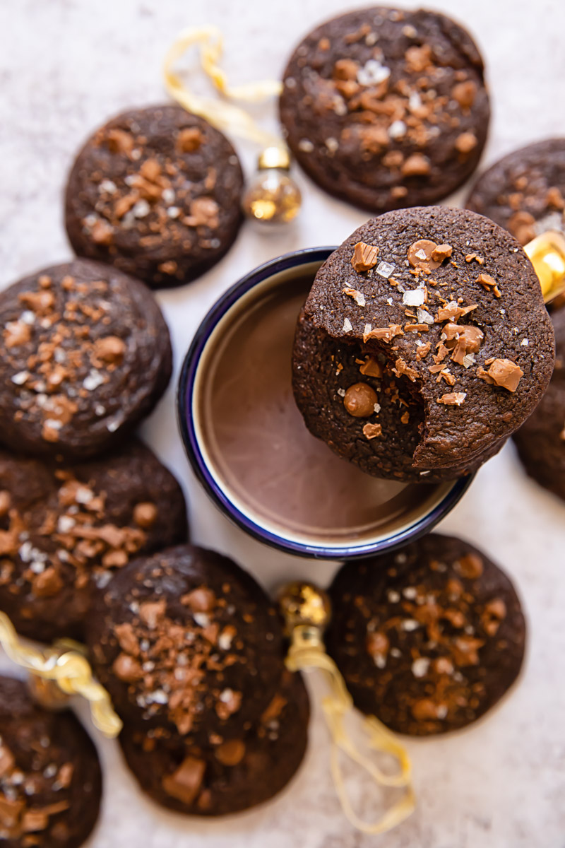 top down view of cookies around a mug with hot chocolate with a half eaten cookie on top of the mug.