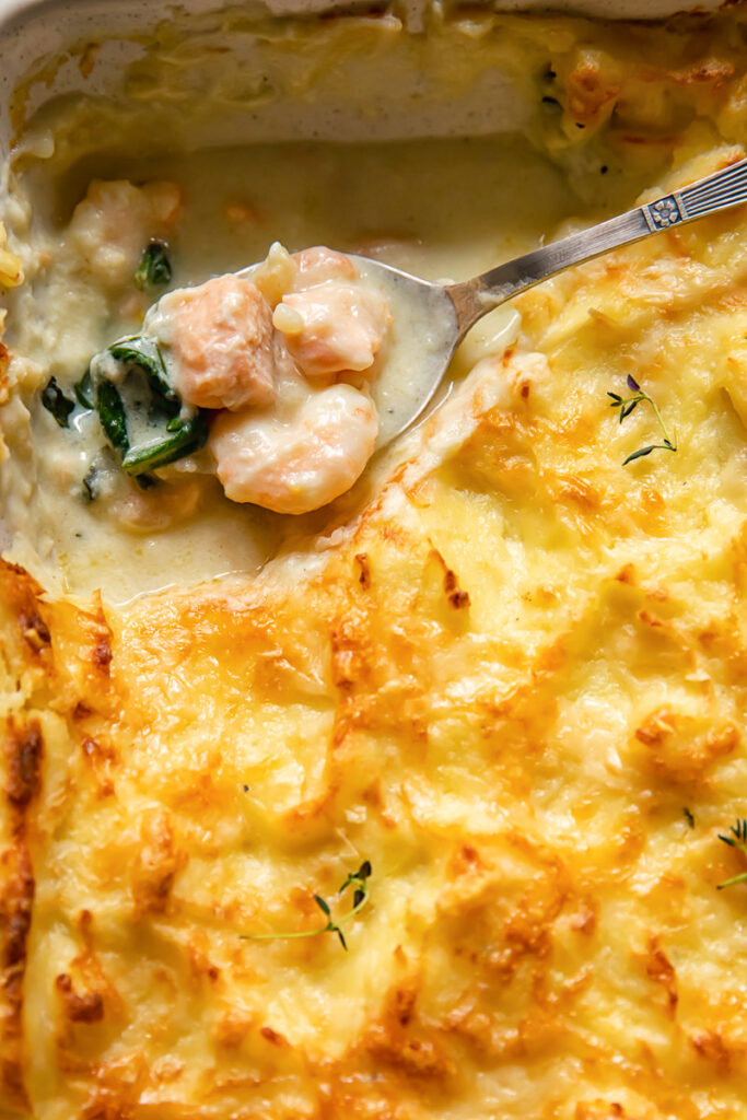 top dow view of fish pie with a spoon holding the creamy filling of fish pieces