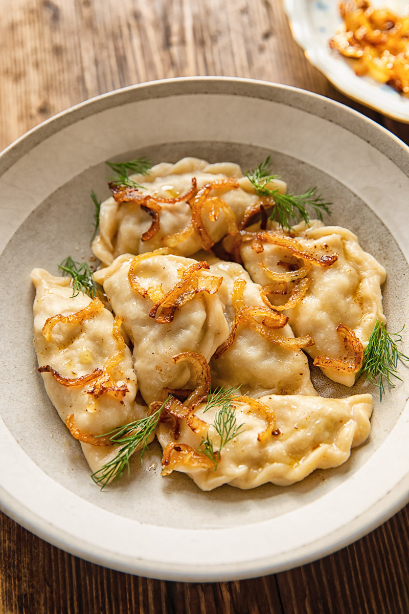 varenyky in a bowl, topped with fried onions and fresh dill