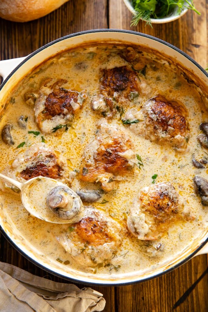 chicken in creamy sauce in a pan, a spoon with a mushroom inside