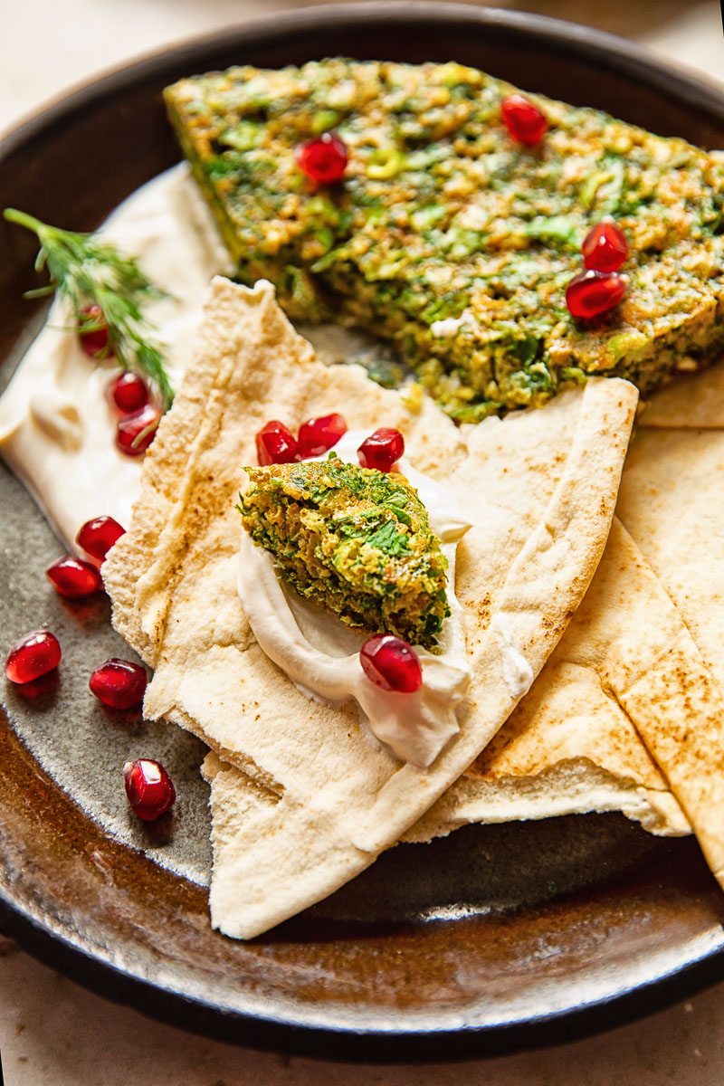 torn flatbread smeared with plain yogurt and a piece of herb frittata on top of it