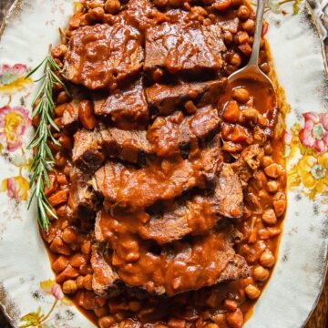 top down view of sliced pot roast with vegetables and chickpeas on a platter