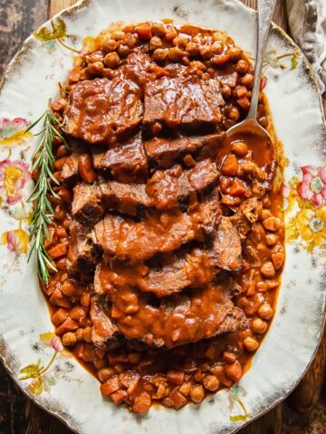 top down view of sliced pot roast with vegetables and chickpeas on a platter