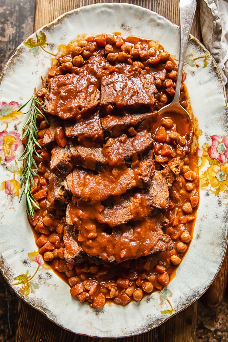 top down view of sliced pot roast with vegetables and chickpeas on a platter