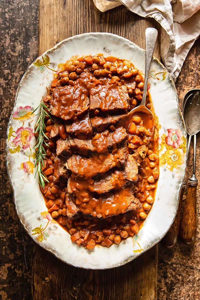 top down view of sliced roast beef with a tomato based gravy and chickpeas