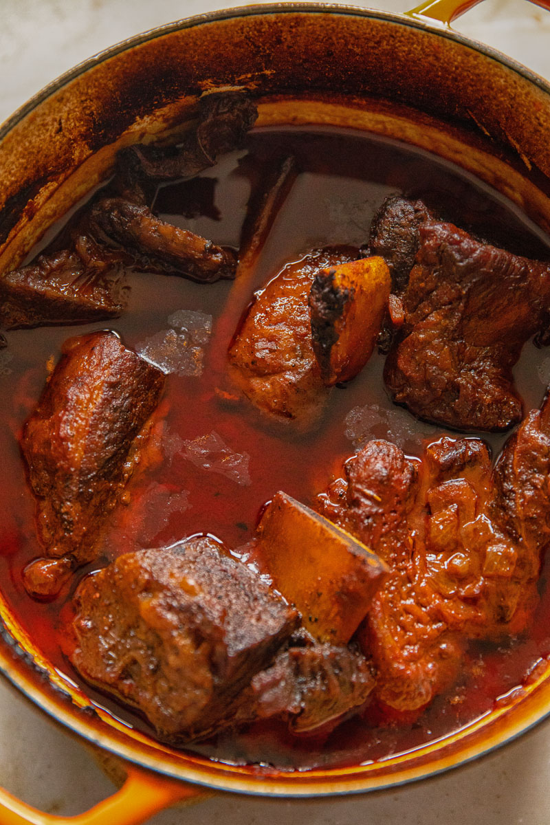 cooked short ribs in red liquid in a large pan