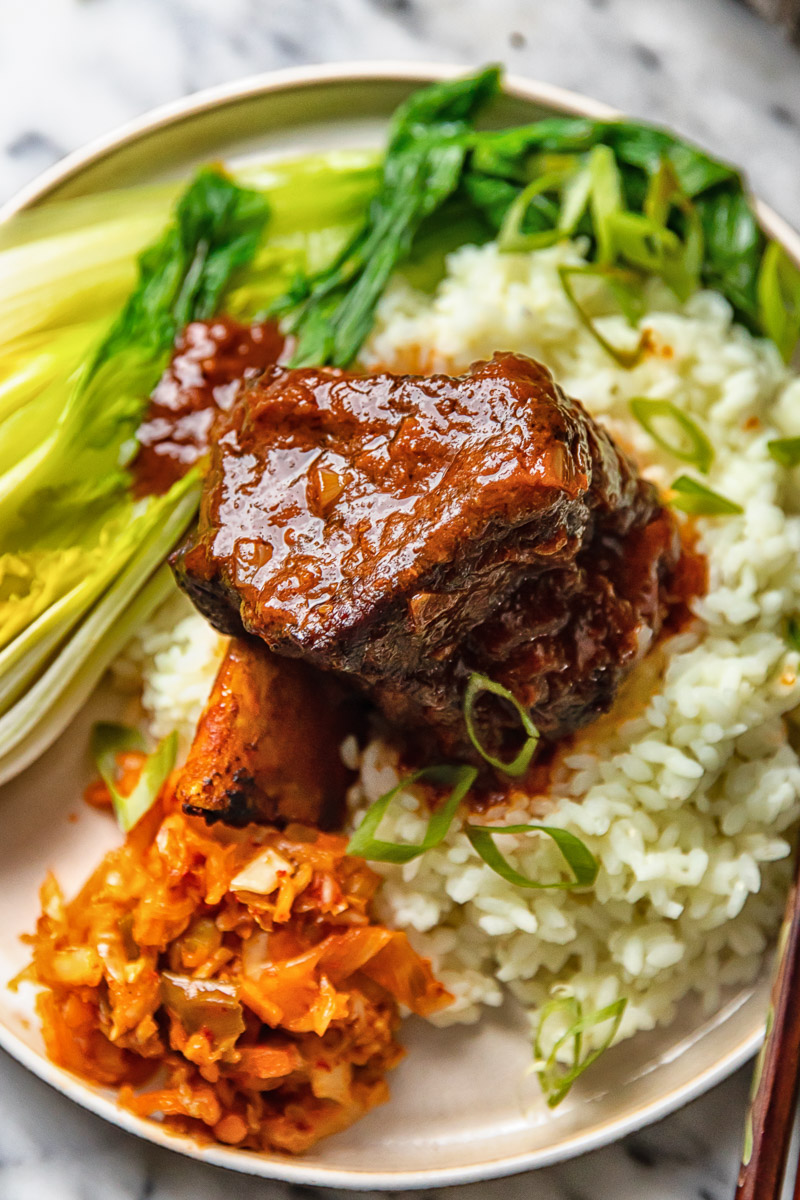 short rib on a bed of rice with bok choy and kimchi on a plate