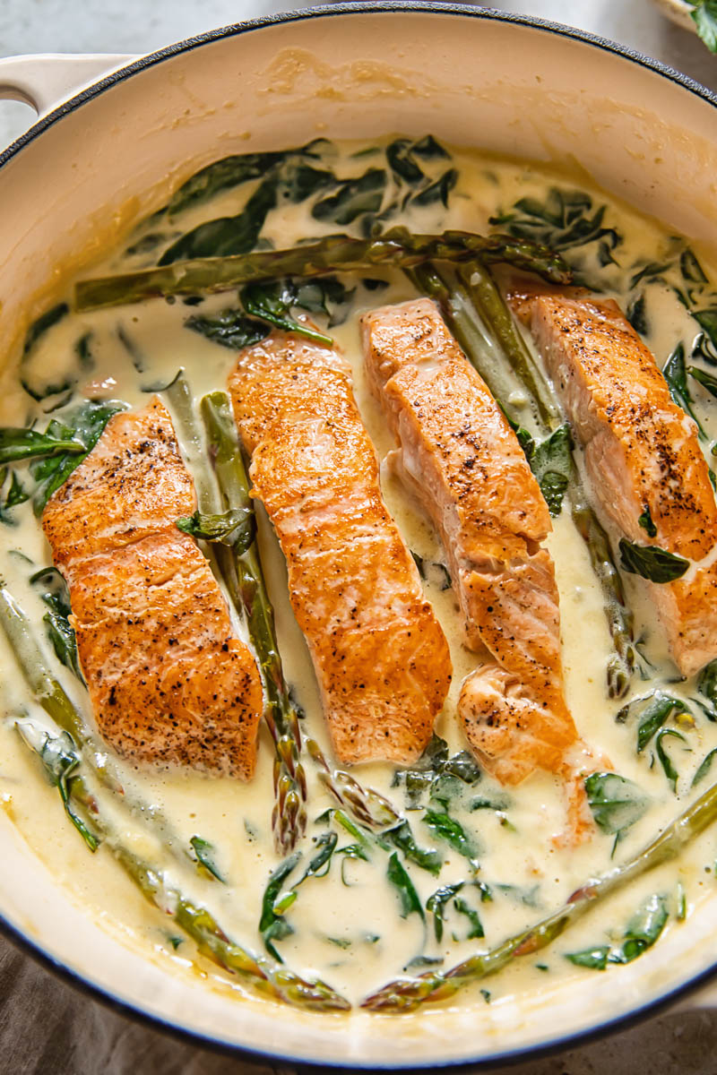 salmon in a pan with creamy sauce and greens