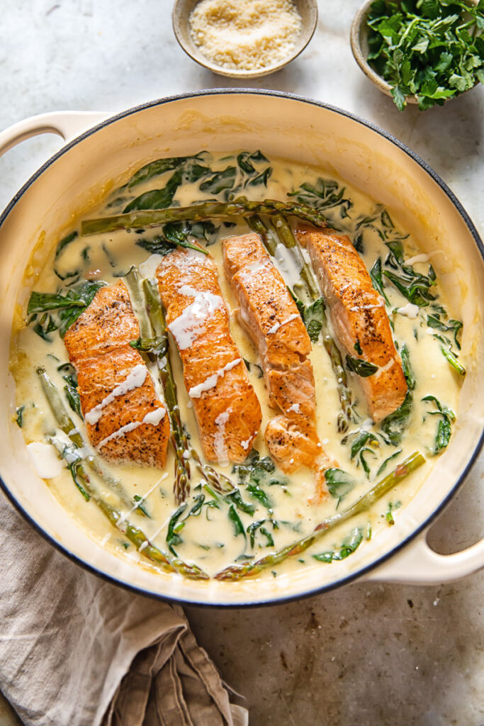 top down view of salmon filets in a creamy sauce with spinach and asparagus