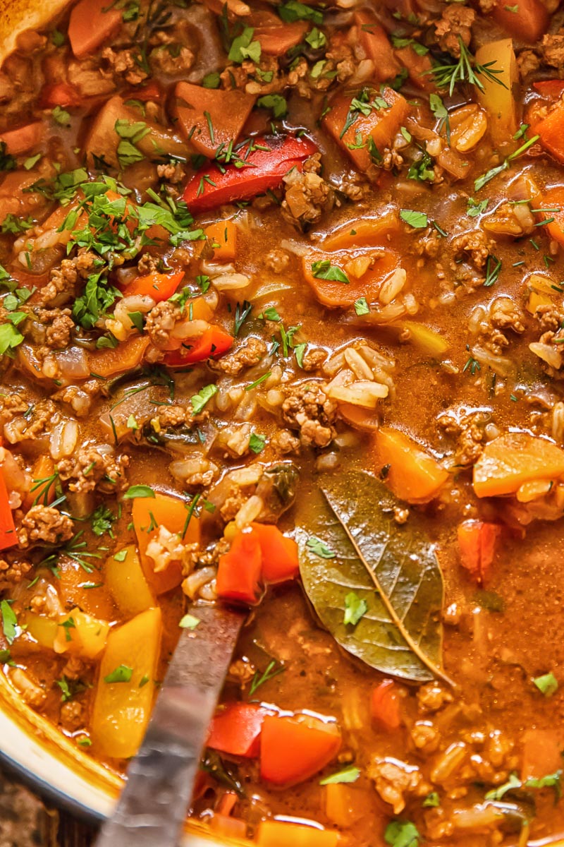 close up of a soup with ground beef and rice in a pot with a ladle in it