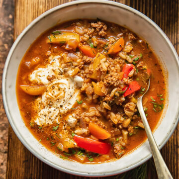 top down view of soup in a bowl with a spoon in in, a little bowl of chopped herbs next to it