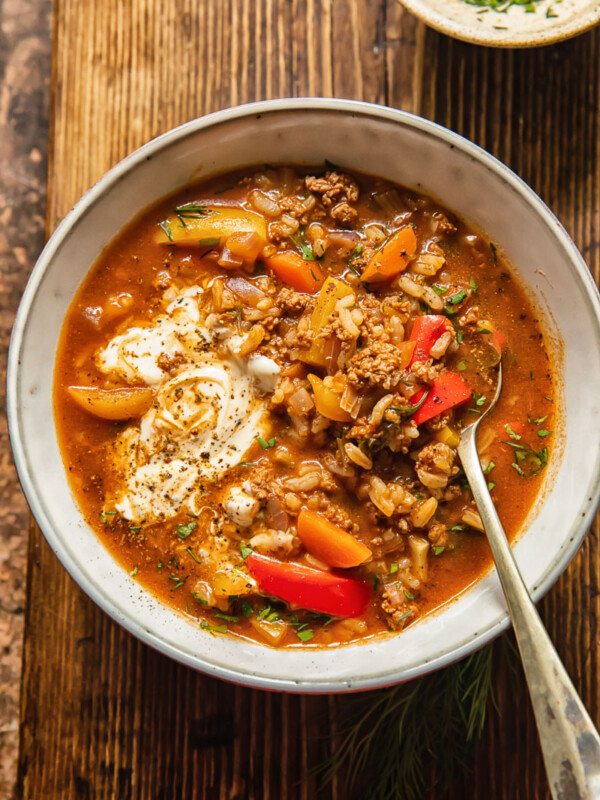 top down view of soup in a bowl with a spoon in in, a little bowl of chopped herbs next to it
