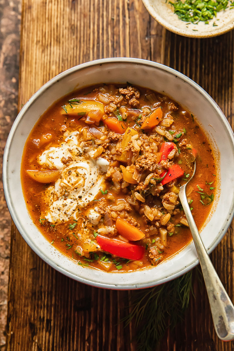 top down view of soup in a bowl with a spoon in in, a little bowl of chopped herbs next to it