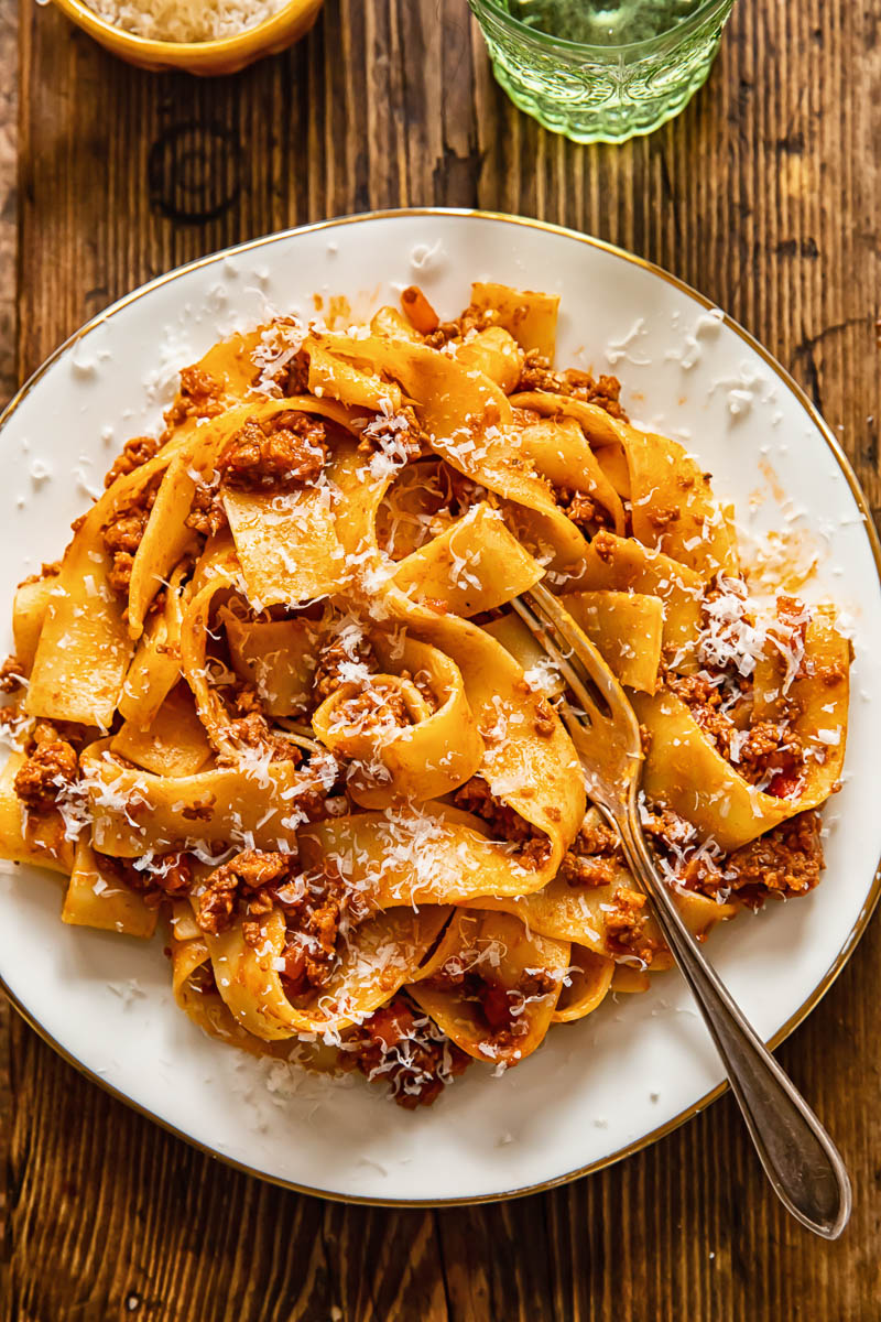 top down view of pappardelle pasta with sauce on a white plate.