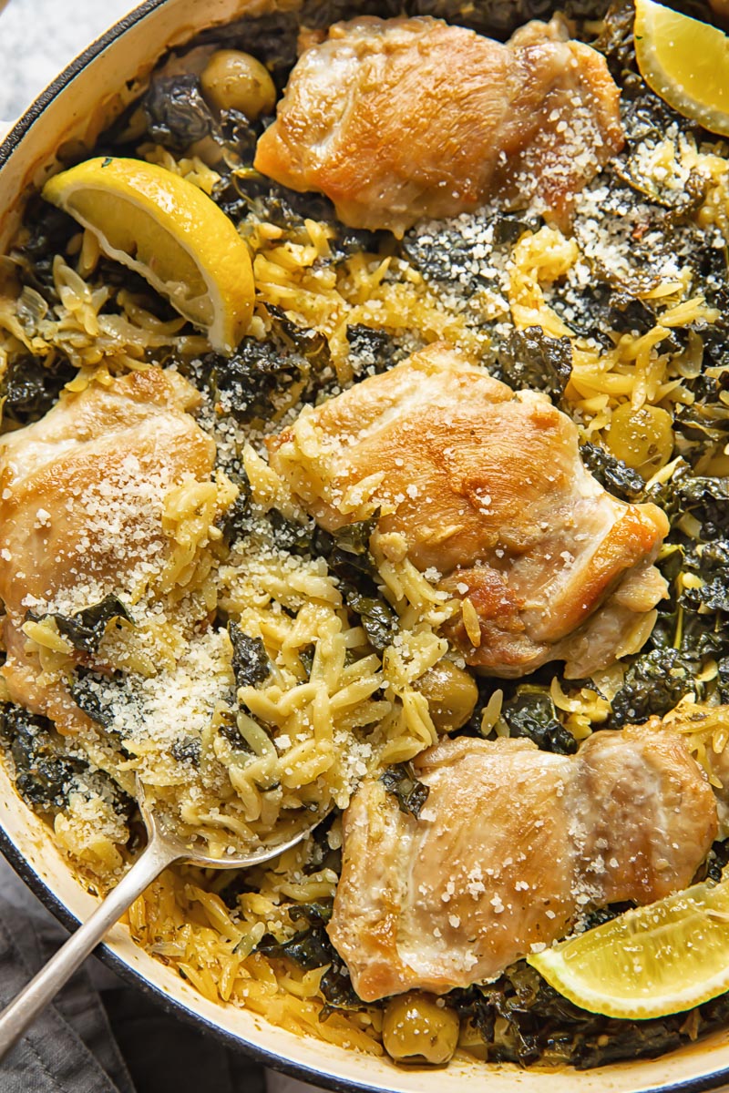 top down view of cooked chicken thighs on top of orzo with kale in a pan