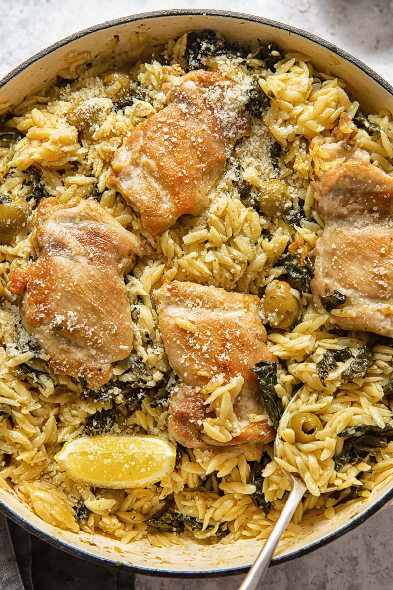 basil pesto orzo with chicken thighs and lemon wedges in a cast iron pan