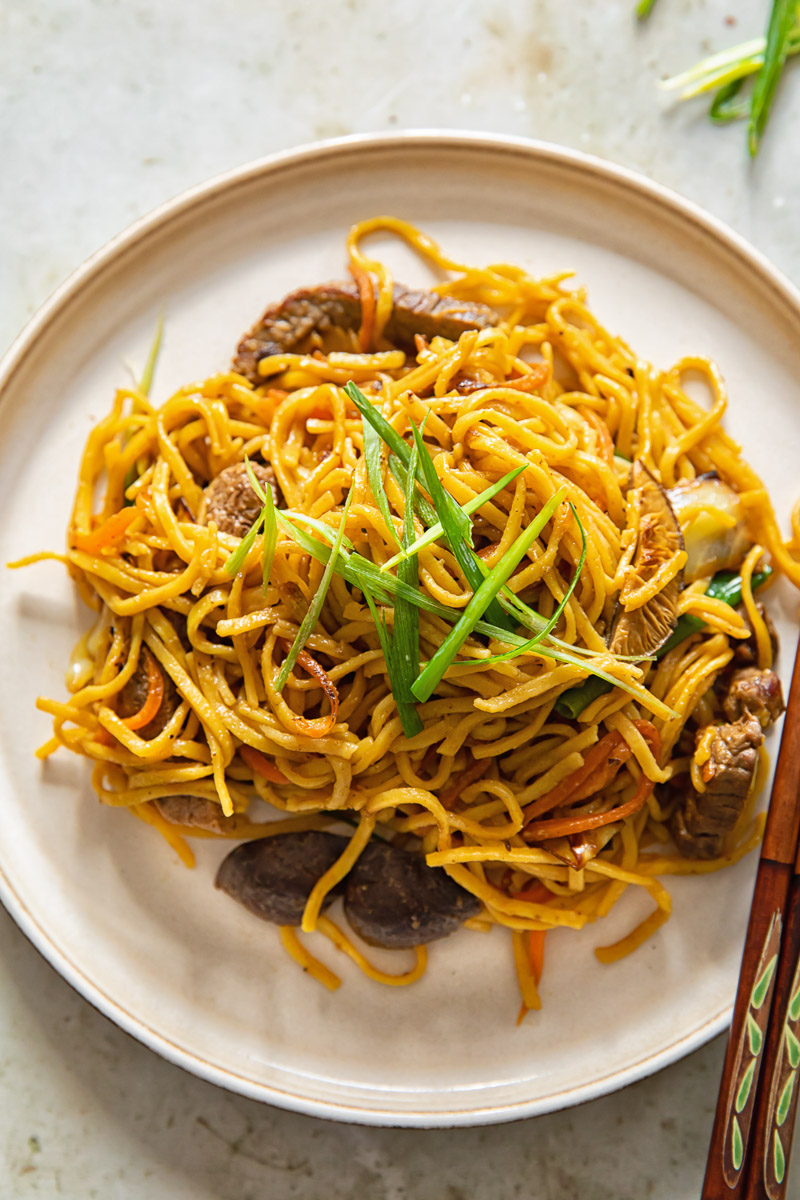 noodles topped with sliced green onions on a brown plate