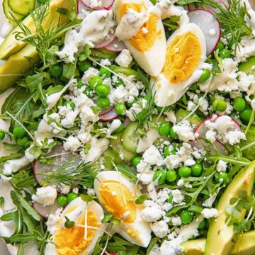 top down view of a salad on a platter topped with boiled egg wedges, peas, feta and avocado