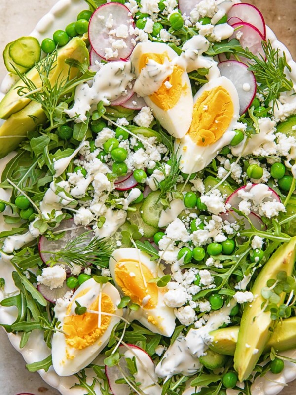 top down view of a salad on a platter topped with boiled egg wedges, peas, feta and avocado