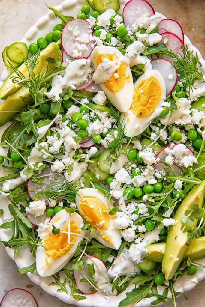 top down view of a salad on a platter topped with boiled egg wedges, peas, feta and avocado
