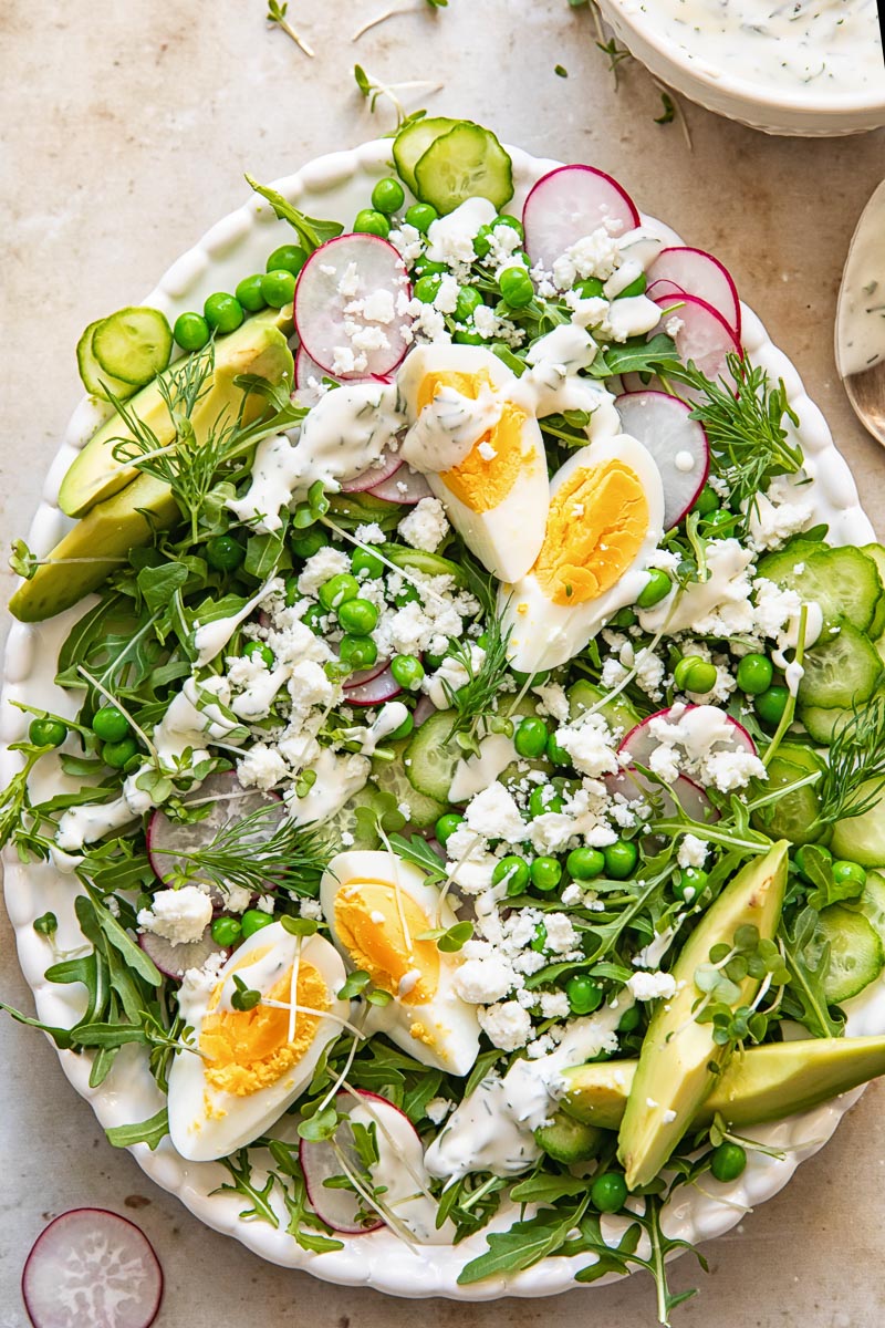 top down view of a salad topped with green peas, boiled eggs, sliced radishes and avocado