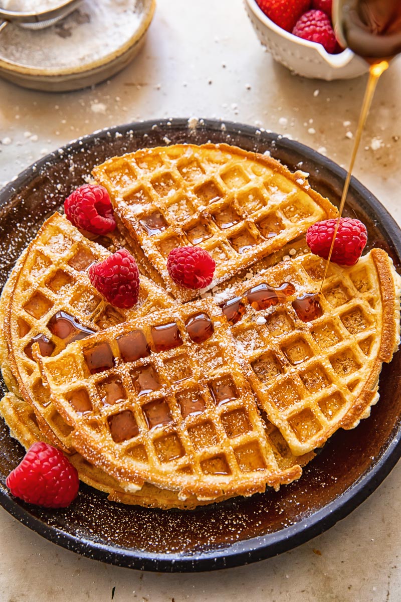maple syrup being frizzled over waffles topped with raspberires