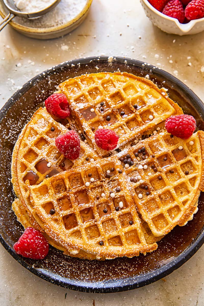 round Belgian waffles topped with raspberries, icing sugar and sprinkles