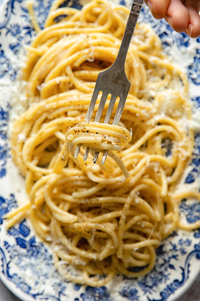 a few bucatini strands over a fork, a platter of pasta in the background